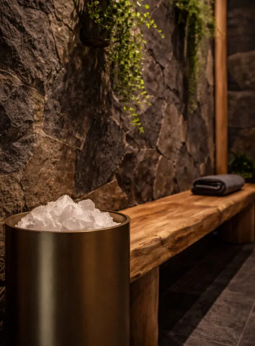 Strefa SPA z metalową misą, drewnianą ławą z ręcznikiem i kamienną ścianą w tle.